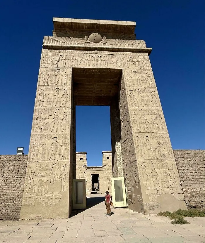 Ancient Egypt stone gateway with intricate hieroglyphs and carvings under clear blue sky, showcasing historical architecture.