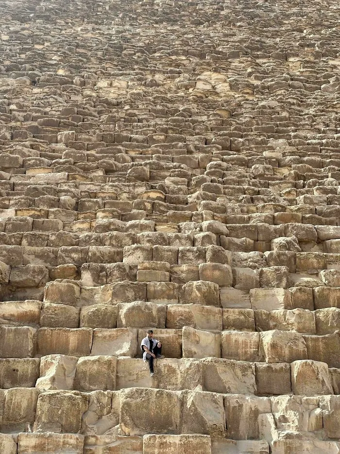 Person sitting on large ancient stones of a pyramid wall, showcasing incredible photographs from Ancient Egypt history.