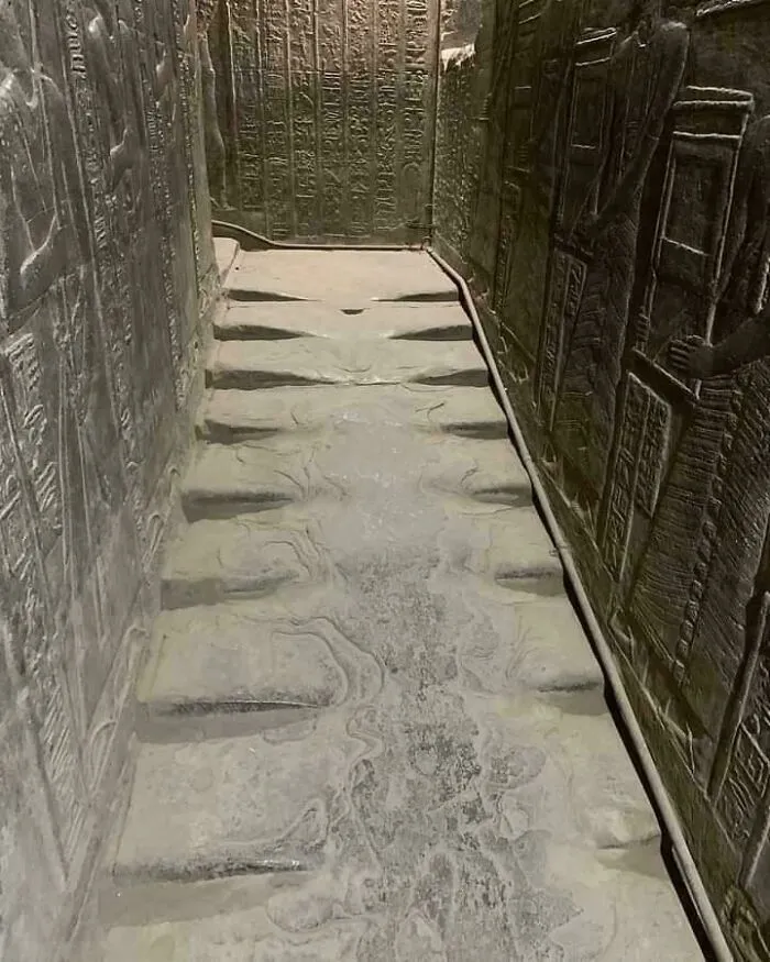 Ancient Egypt stone floor with carved grooves surrounded by hieroglyphs and wall reliefs inside historic tomb.