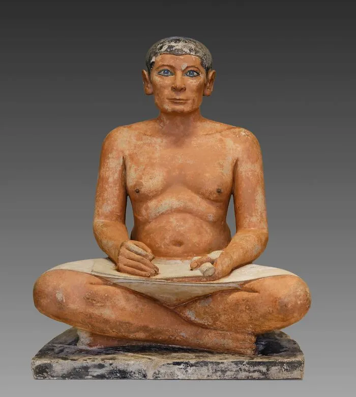 Ancient Egypt statue of a seated scribe holding a papyrus scroll, showing detailed craftsmanship and lifelike features.