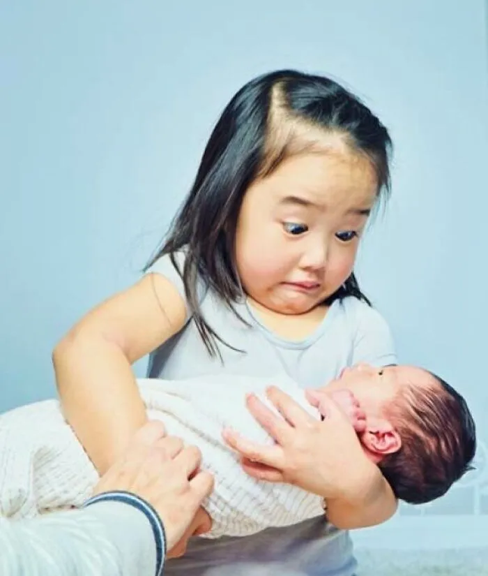 Heartwarming photo of a young girl holding a newborn baby with a surprised and tender expression.