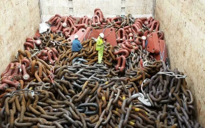 Two workers in helmets standing on a massive pile of heavy industrial chains causing fear for those with megalophobia.