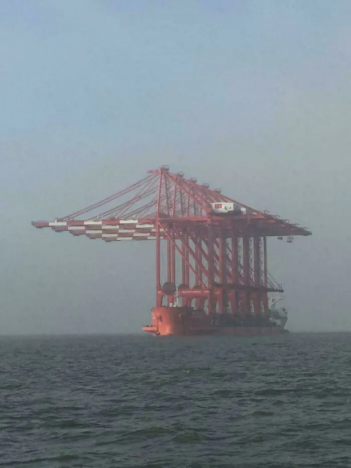 Massive red shipping crane structure on a cargo ship in the ocean, evoking fear in those with megalophobia.