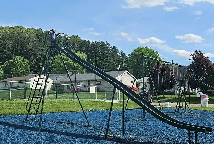 Young child climbing a tall slide at a playground, capturing a wholesome and funny dad moment outdoors.
