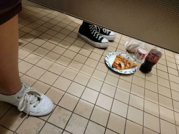 Shoes and a plate with pizza and drinks placed on a bathroom floor in a Walmart store, unusual in-store scene.