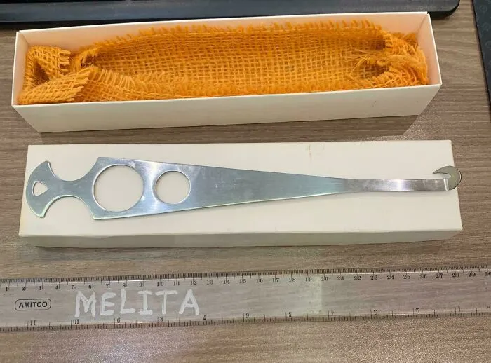 Metal tool with circular cutouts and hook, placed on a box and table with ruler, one of the bizarre Christmas gifts received.