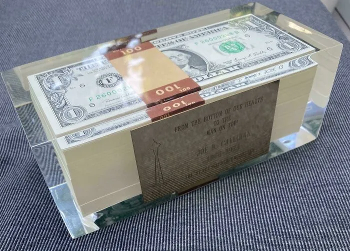 Stack of fake $100 bills encased in clear resin, a bizarre Christmas gift idea on a fabric surface.