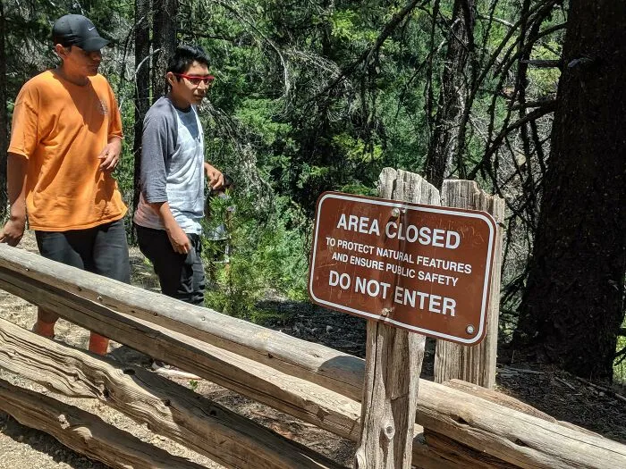 Dos personas ignoran cartel de área cerrada en bosque, un claro ejemplo de comportamiento irrespetuoso y ser un maleducado.