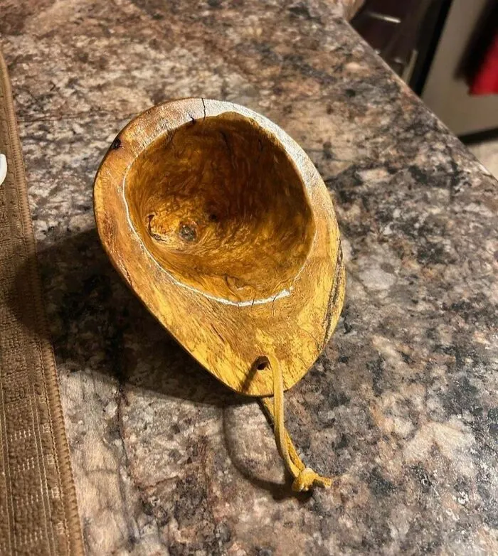 Hand-carved wooden bowl with leather strap placed on a kitchen countertop, one of the most bizarre Christmas gifts received.