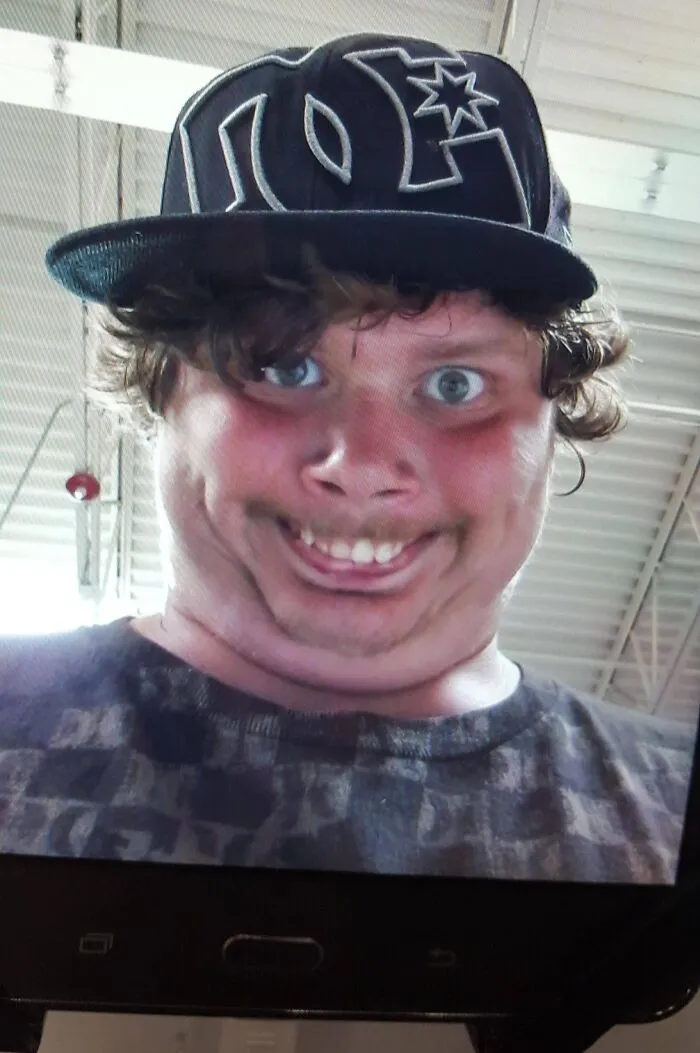 Close-up selfie of a young man with a distorted face wearing a DC hat inside a Walmart store environment.