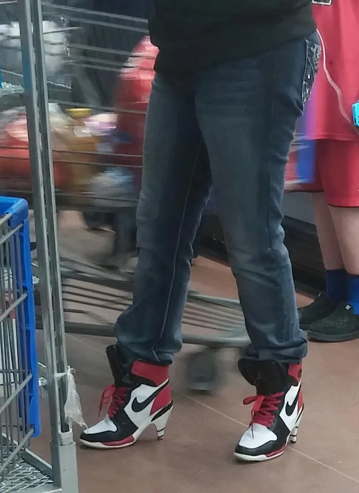 Person wearing Nike high-heeled sneakers and jeans standing near a shopping cart inside a Walmart store.
