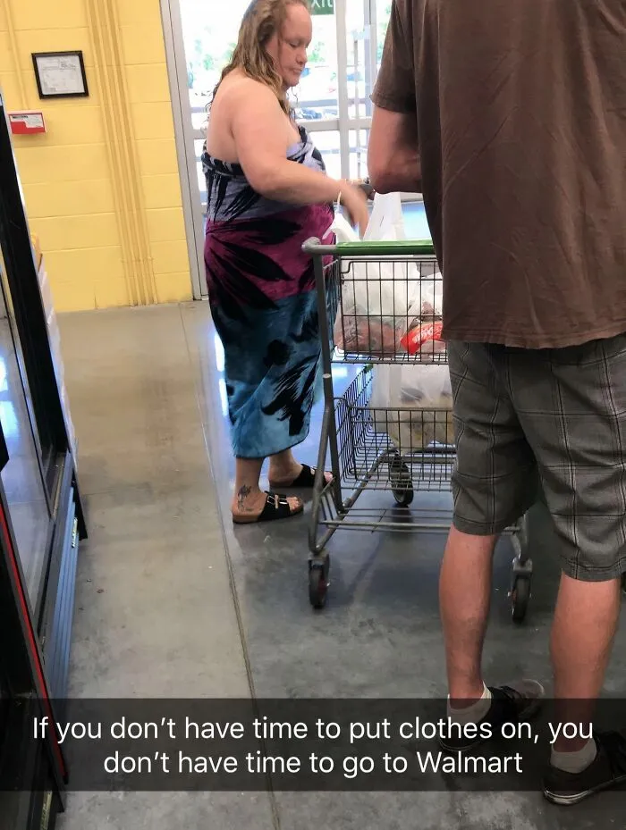 Woman shopping at Walmart in a towel dress, pushing a cart while a man stands nearby inside the store.