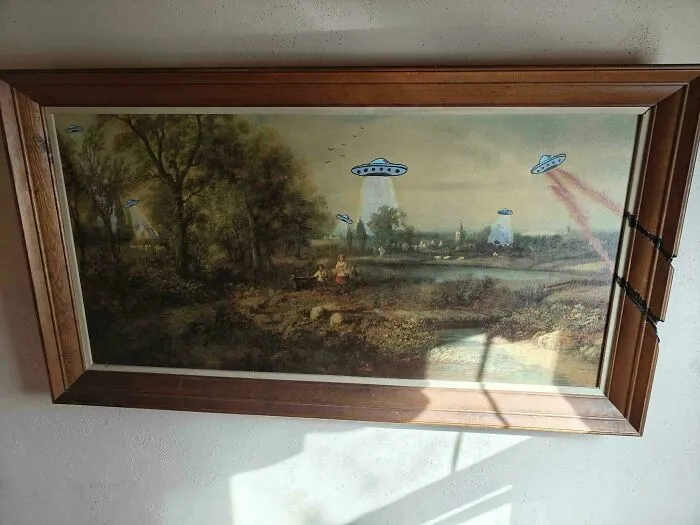 Thrifted painting of a countryside scene humorously altered with UFOs beaming light in a playful unexpected twist.