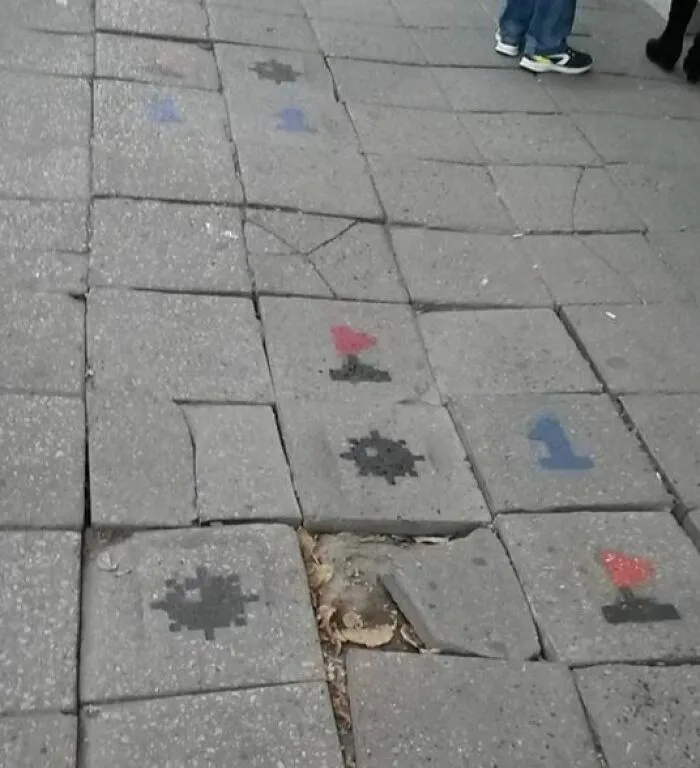Worn and cracked sidewalk tiles with faded painted game markings common in Eastern Europe streets.