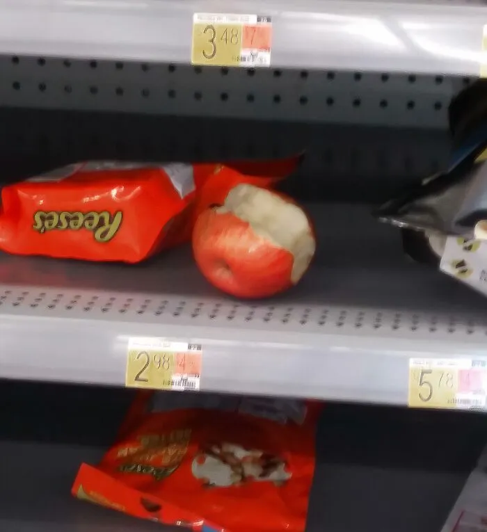 Next-level jerks: half-eaten apple abandoned on store shelf beside Reese's candy.