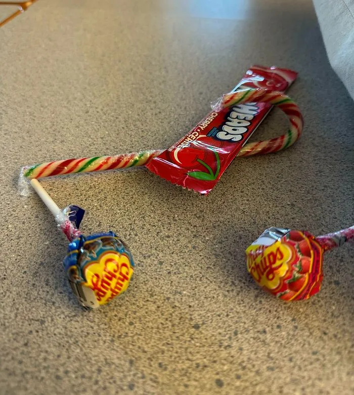 Candy assortment including two Chupa Chups lollipops, a candy cane, and a Cherry Sours, example of bad Secret Santa gifts.