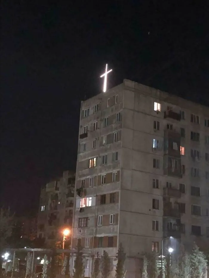 Apartment building at night with a glowing cross on the roof, showcasing Eastern Europe humor and culture in a meme style.