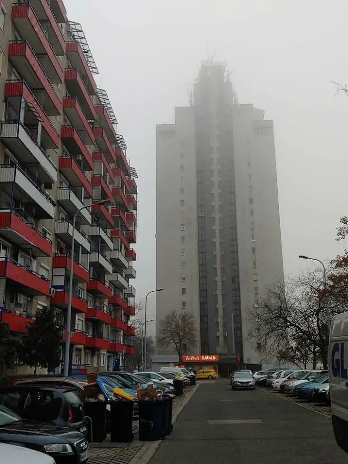 Foggy urban scene with Eastern Europe apartment buildings, parked cars, and visible trash bins along the street.