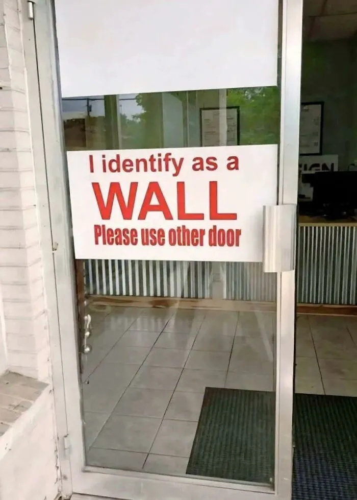 Funny meme on a glass door with red text saying I identify as a wall, asking to use the other door.
