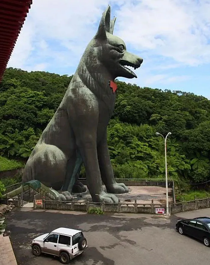 Giant dog statue in a parking area surrounded by greenery, showcasing one of the weirdest buildings worldwide.