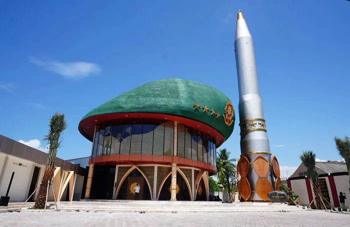 Bread-shaped bread factory building with a unique dome design and a tall rocket sculpture beside it under a clear sky.