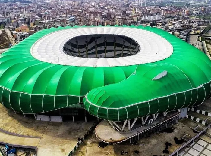 A large green stadium shaped like a snake viewed from above in an urban area featuring unique architectural design.