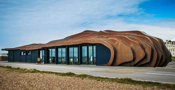 Bread-shaped bread factory with a modern design and rust-colored exterior located in an open urban area under blue sky.