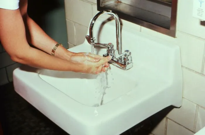 Person washing hands under running water in a white sink, illustrating a public speaking or deep water dilemma concept.