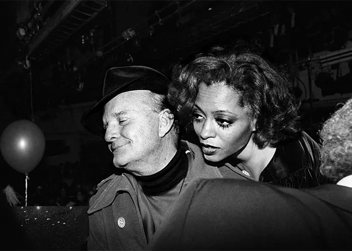Black and white rare pop culture photo of two people close together at a crowded indoor event with a balloon in the background.