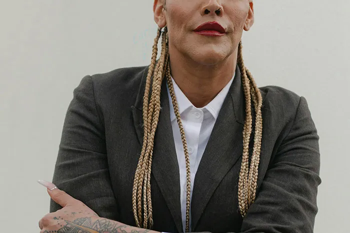 Person with braided hair and tattoos wearing a dark blazer, representing deepest secrets people refuse to reveal to parents.