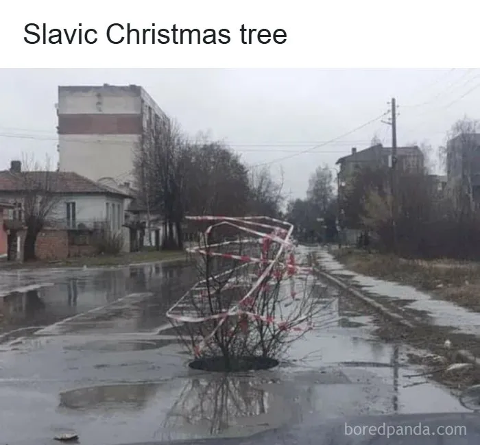 A small tree wrapped with red and white tape stuck in a large pothole on a wet street in Eastern Europe.