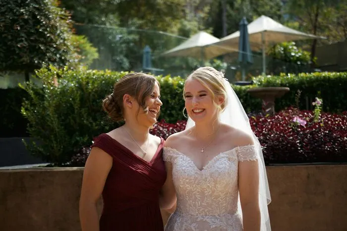 Two women, one in a wedding dress and the other in a burgundy dress, smiling during an outdoor event about painful divorce.
