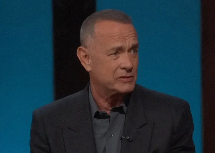 Actor in a dark suit sharing insights on famous people they've met during an interview or discussion setting.