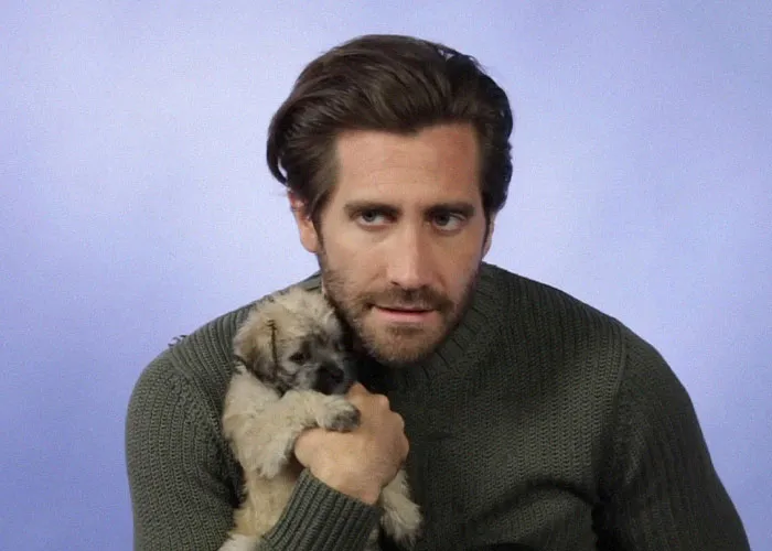 Man in green sweater holding a small puppy, sharing candid moments about famous people they have met.