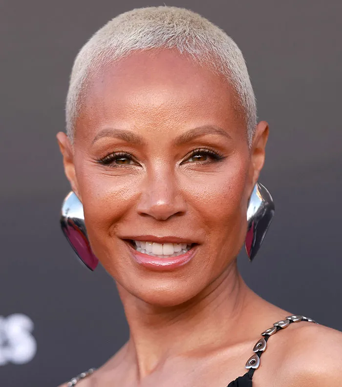 Close-up of a smiling celebrity with short blonde hair and silver earrings, featured in most disliked celebrities 2025 list.
