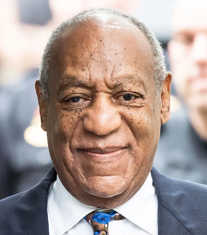 Close-up of a disliked celebrity in 2025, smiling slightly while wearing a suit and patterned tie outdoors.