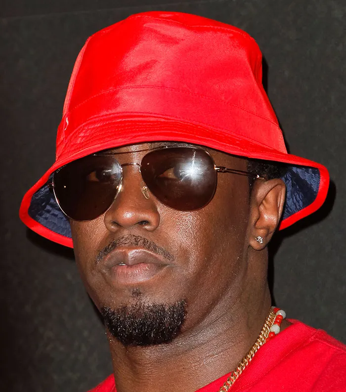 A man wearing a red bucket hat and sunglasses, representing the most disliked celebrities of 2025.