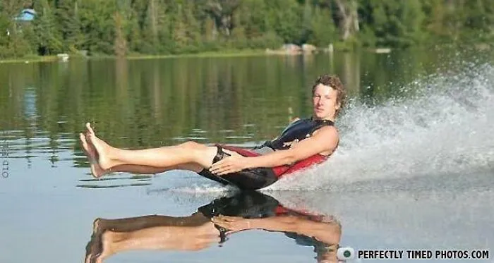 Man water skiing with perfect timing, captured mid-glide creating a clear reflection on the lake surface.