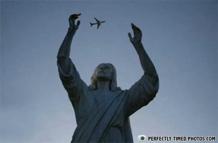 Statue with arms raised appearing to catch an airplane flying overhead in a perfectly timed photo.