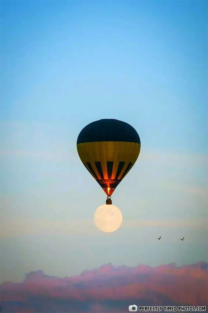 Hot air balloon perfectly timed to appear as if holding the rising full moon above colorful clouds in an impressive photo.