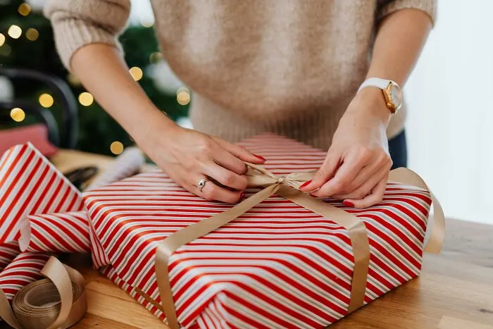 Person tying ribbon on a striped Christmas gift, illustrating the concept of horrible gifts people’d rather not receive.
