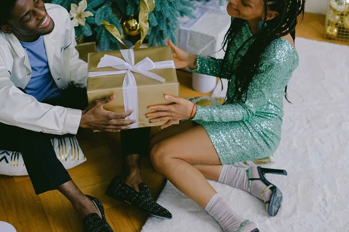 Couple exchanging wrapped Christmas gift near tree, highlighting the idea of horrible holiday presents to avoid.