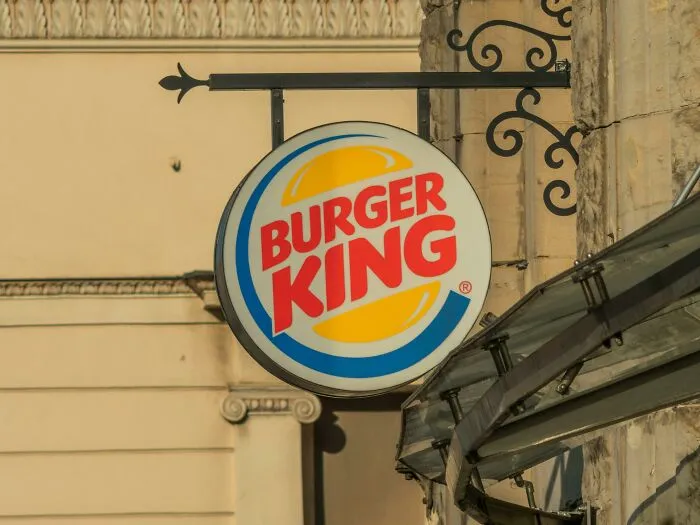 Burger King round hanging sign attached to a building exterior with decorative iron bracket in daylight.