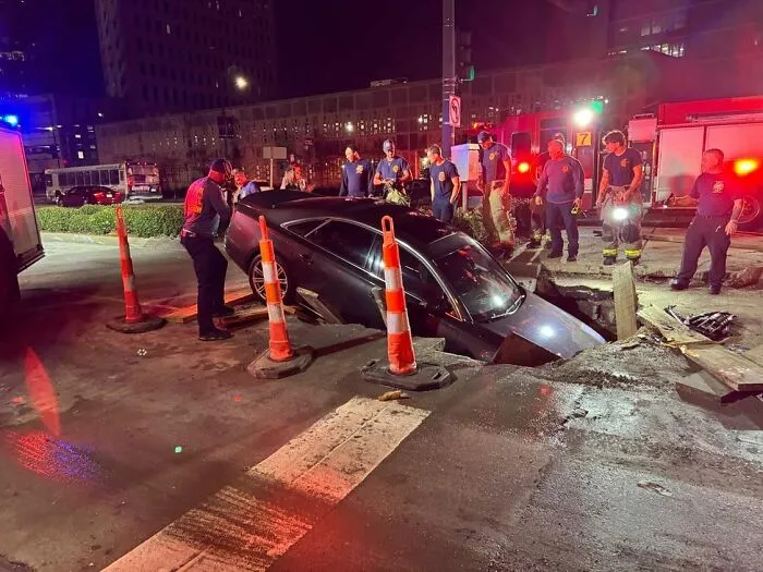 Black car sunk into the street with emergency responders and traffic cones around, showing weirdest things found in streets.