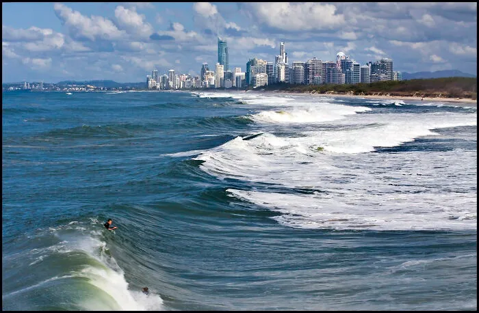 Ocean waves and surfers near a coastal city skyline illustrating disappointing tourist attractions locals still don’t get.