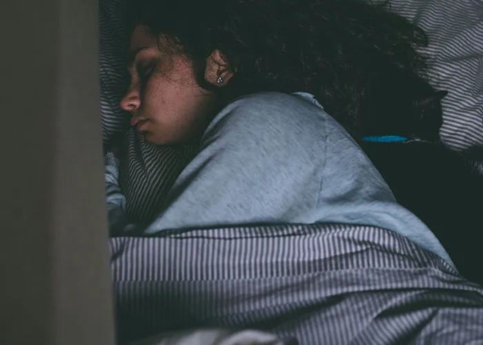 Woman lying in bed with eyes closed, appearing unwell and resting, illustrating medical issues and health struggles.