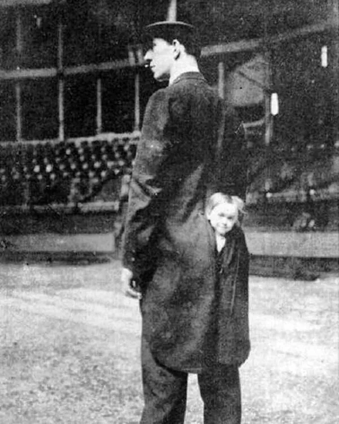 Black and white vintage photo of a man with a child hidden inside his coat, creating an odd and creepy visual effect.