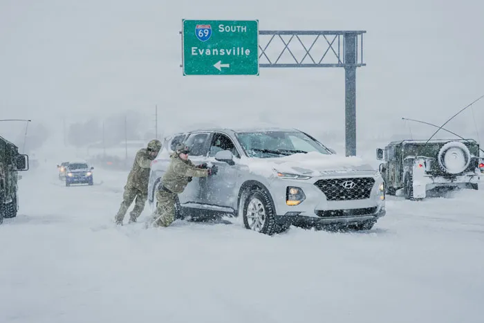Soldiers pushing a white SUV stuck in deep snow during a heavy snowstorm on a highway near Evansville.