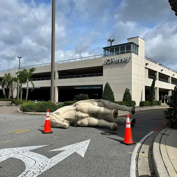 Large fallen statue lying in street near parking garage, surrounded by traffic cones, showing weirdest things found in streets.