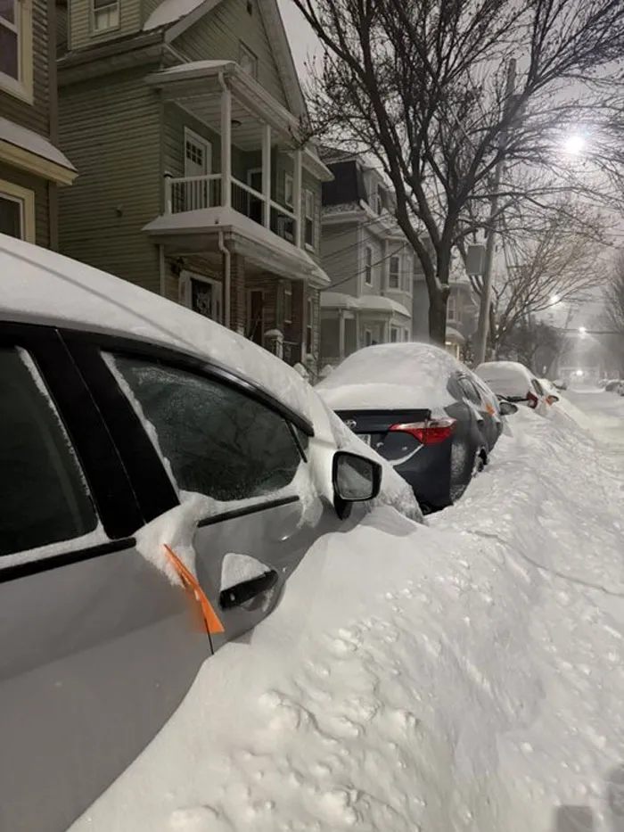 Cars covered in deep snow on a residential street during a heavy snowstorm in the U.S. at night.